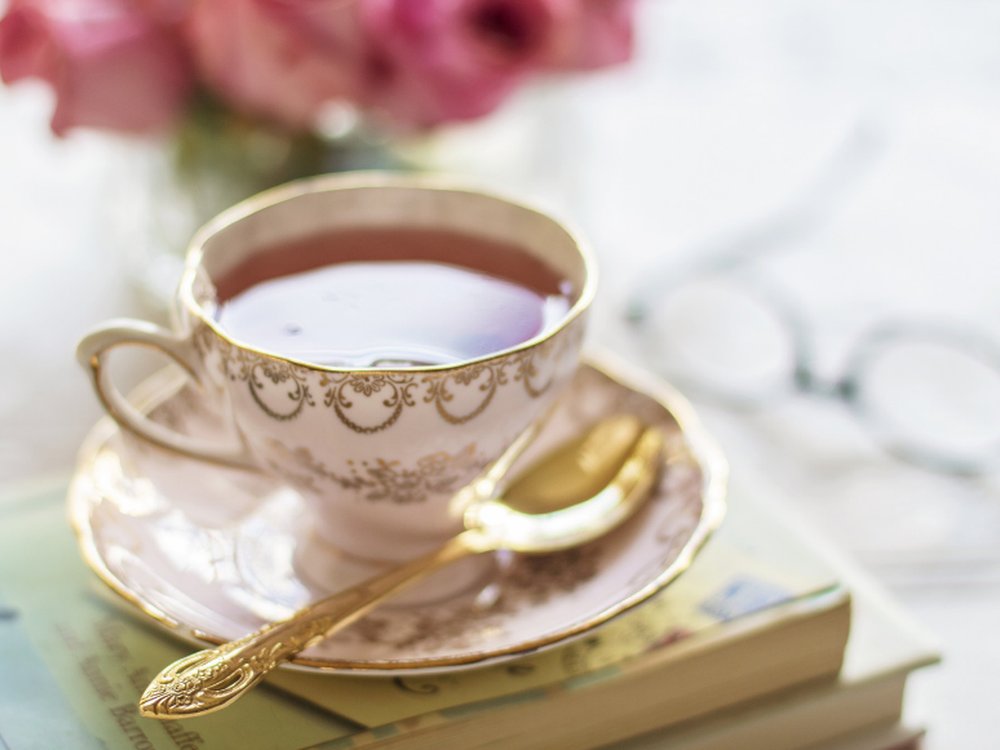 A cup of tea with saucer and teaspoon resting on a stack of books