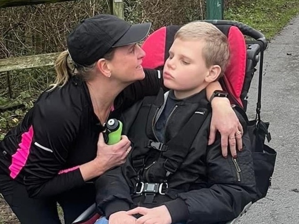 A woman in a baseball cap crouching down with her arm around a boy in a buggy