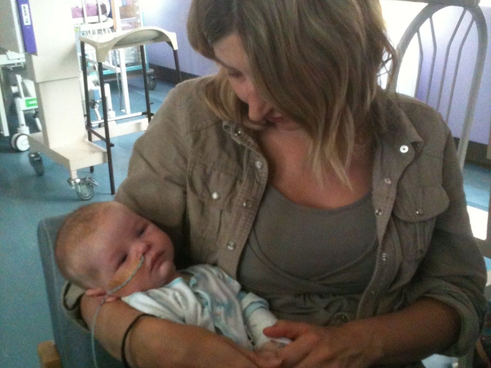 A lady sits in a chair cradling a small baby in a hospital room