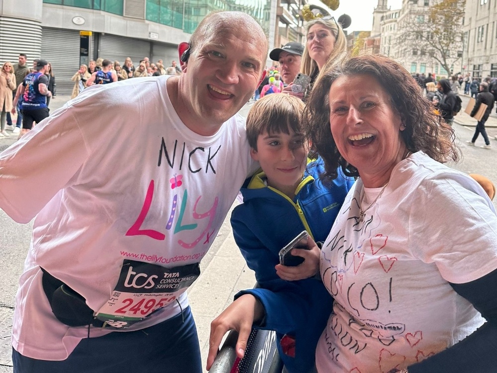 A man wearing a Lily vest and smiling with his arms round his family