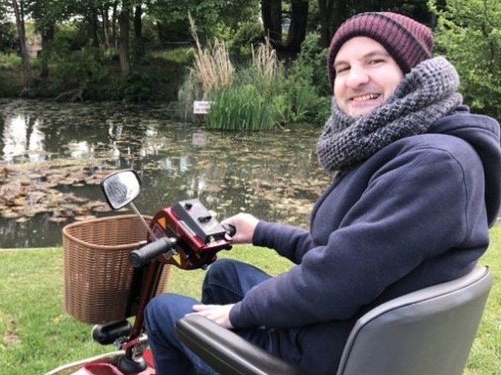 Chris in his wheelchair in front of a pond turning to the camera