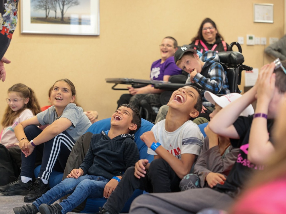 A group of young children sitting on beanbags on the floor are roaring with laughter