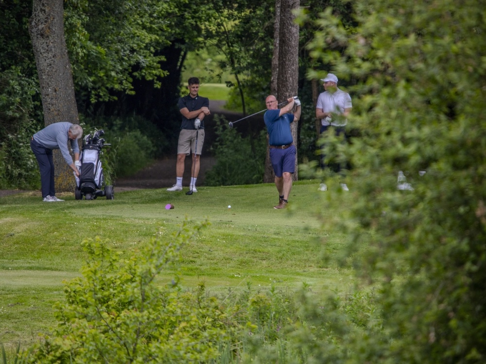 A man swinging a golf course with three other men standing nearby on the course