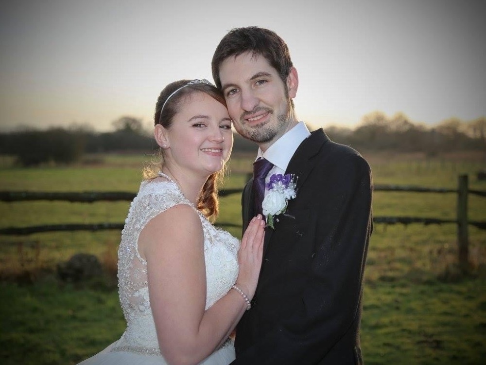 Josey in her wedding dress and husband Chris in suit, tie and buttonhole standing cheek-to-cheek