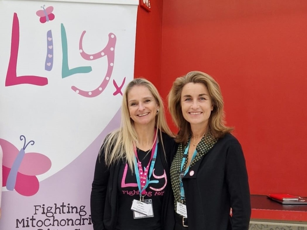 Two women standing side by side in front of a Lily banner