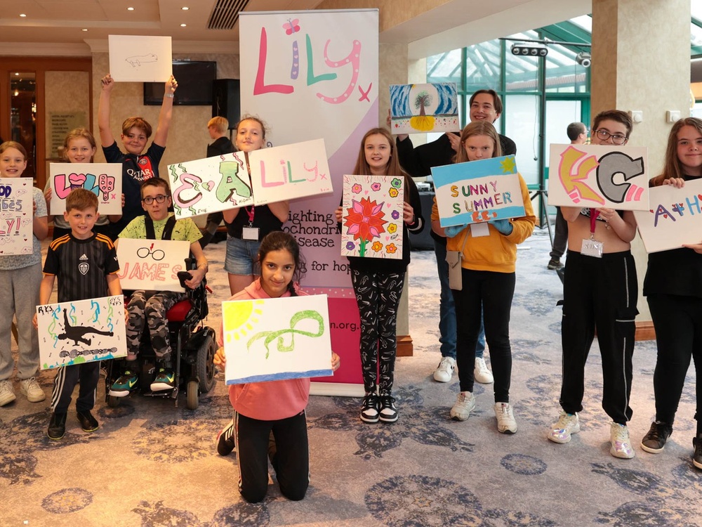 A group of children of varying ages are standing together holding paintings they have done in front of them