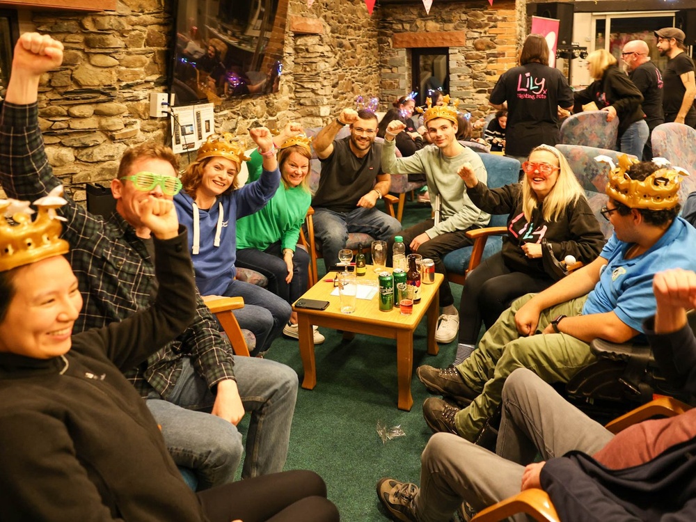 A group of people laughing around a small table wearing inflatable crowns