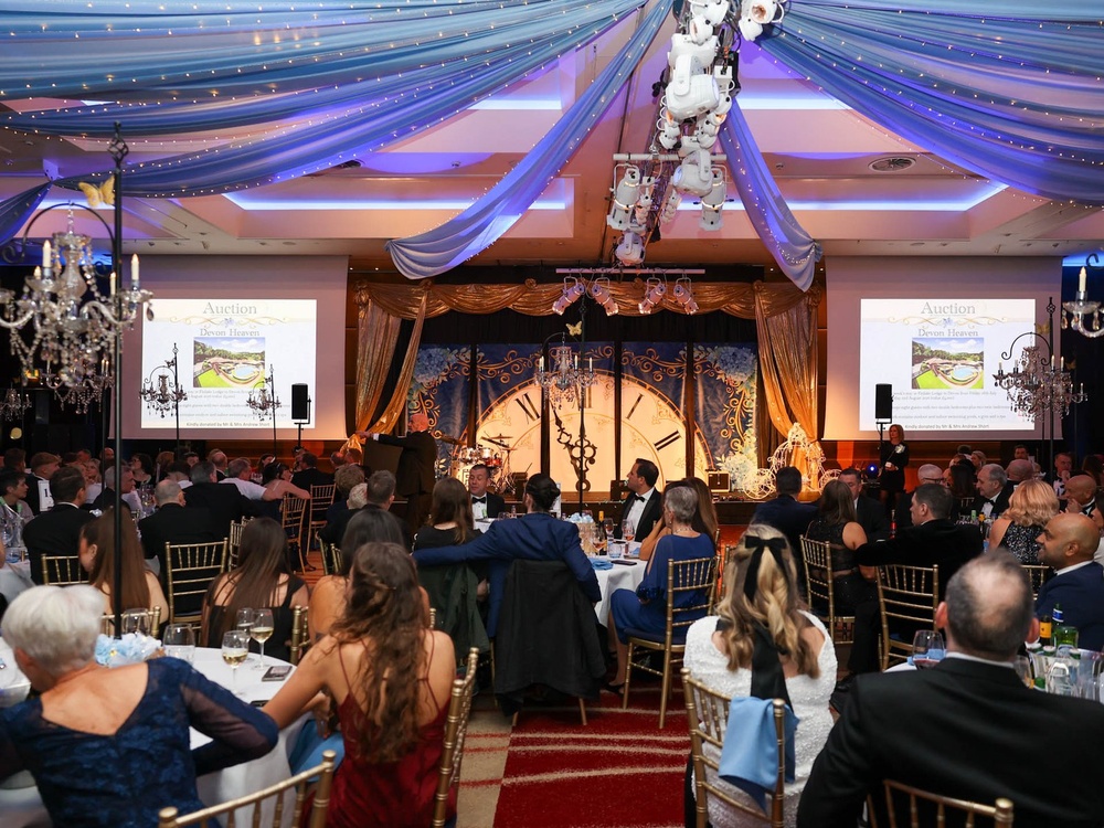 The ballroom at the Lily ball with auction slides showing on screens either side of the main stage