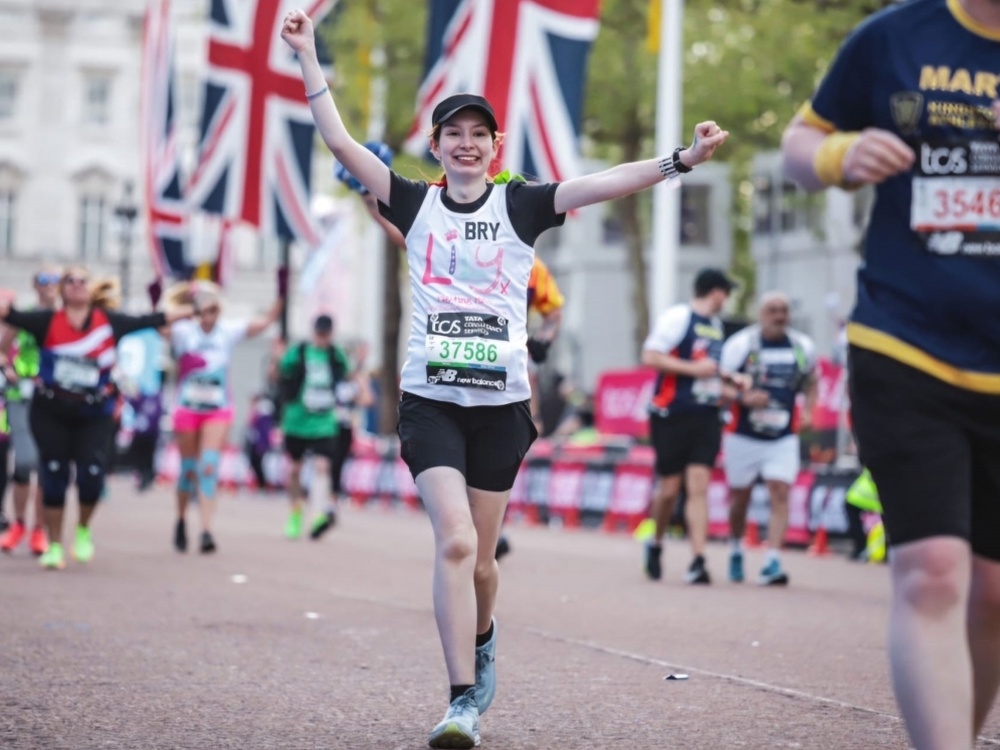 A lady in a Lily Foundation vest smiling and running with her arms in the air