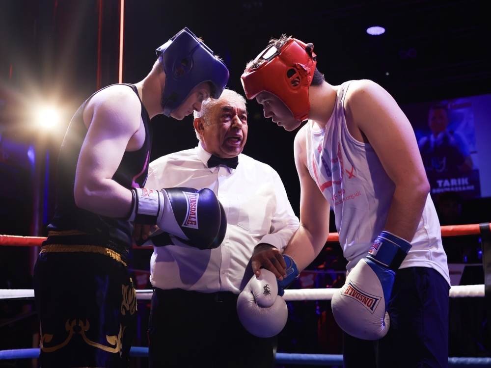 Two boxers lean in as the ref stands between them at the Lily Fight Night