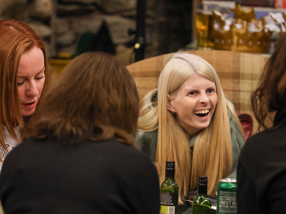 A lady with long blonde hair is roaring with laughter in a group