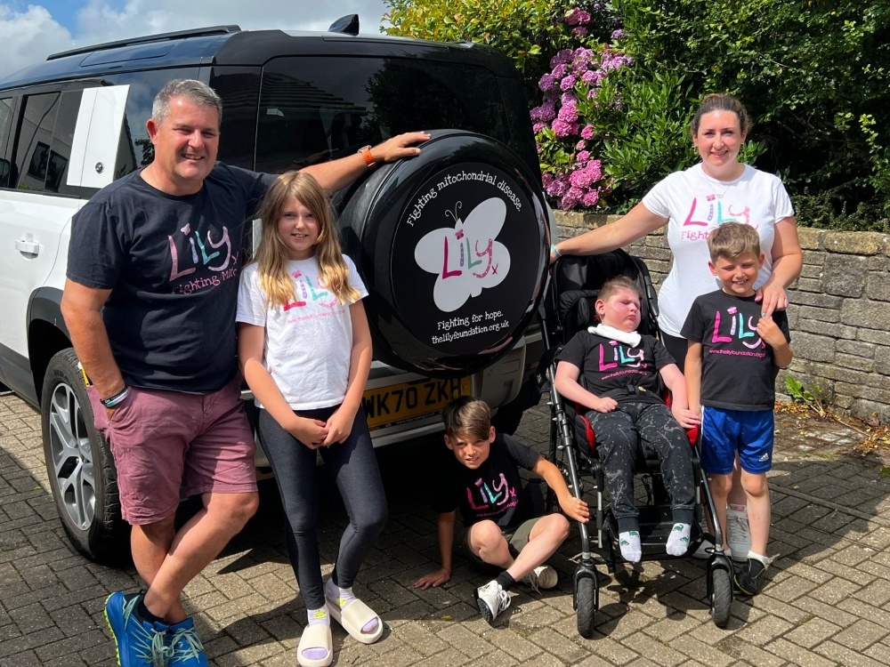 A family standing in front of a Land Rover with a Lily Foundation-branded spare wheel cover