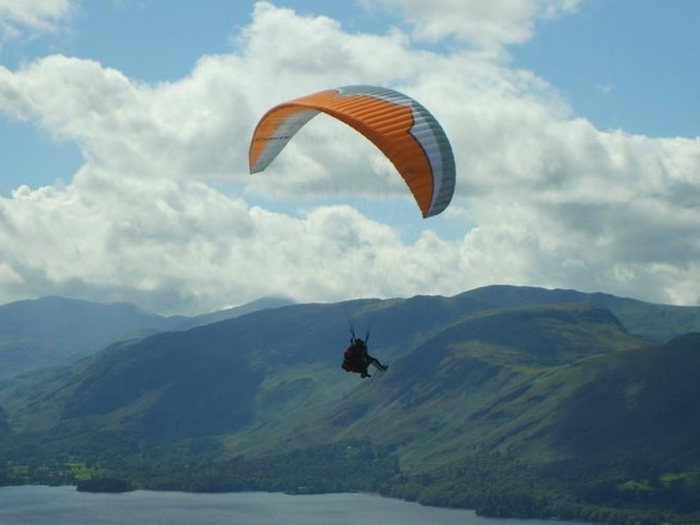 A tandem parapent in progress over a lake surrounded by green hills