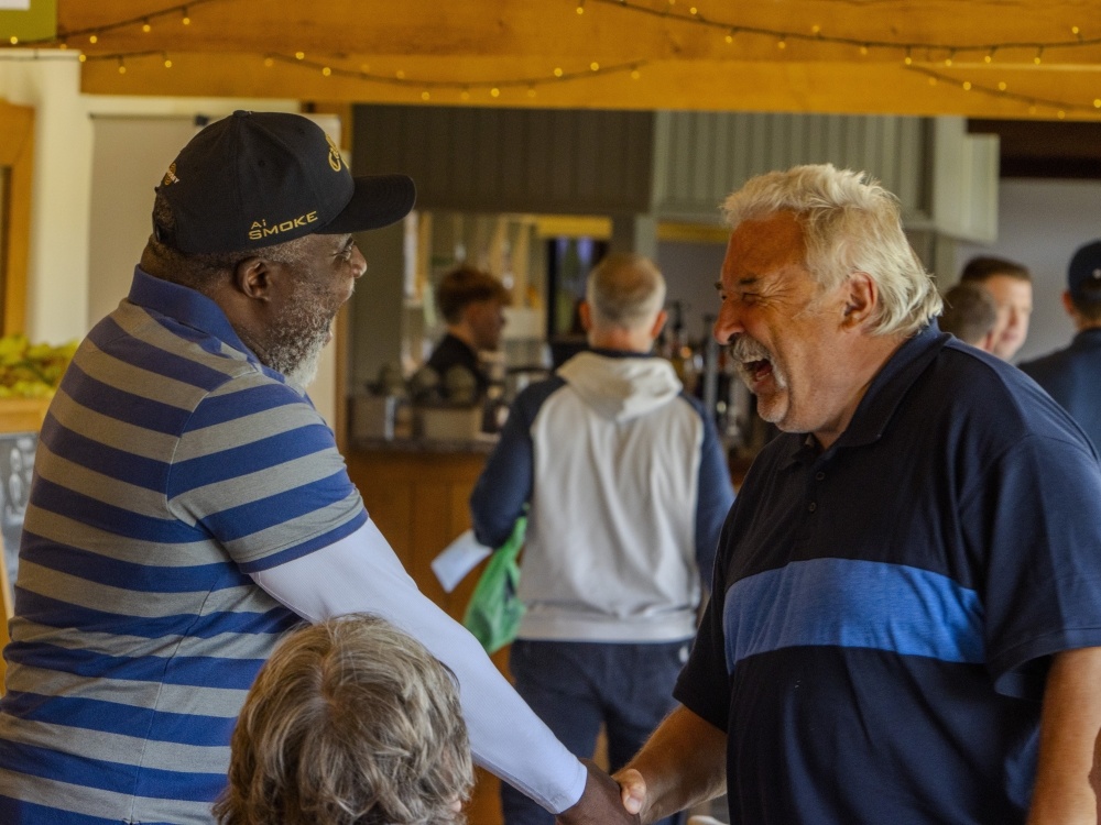 Two men laughing and shaking hands at the Lily South West Golf Day