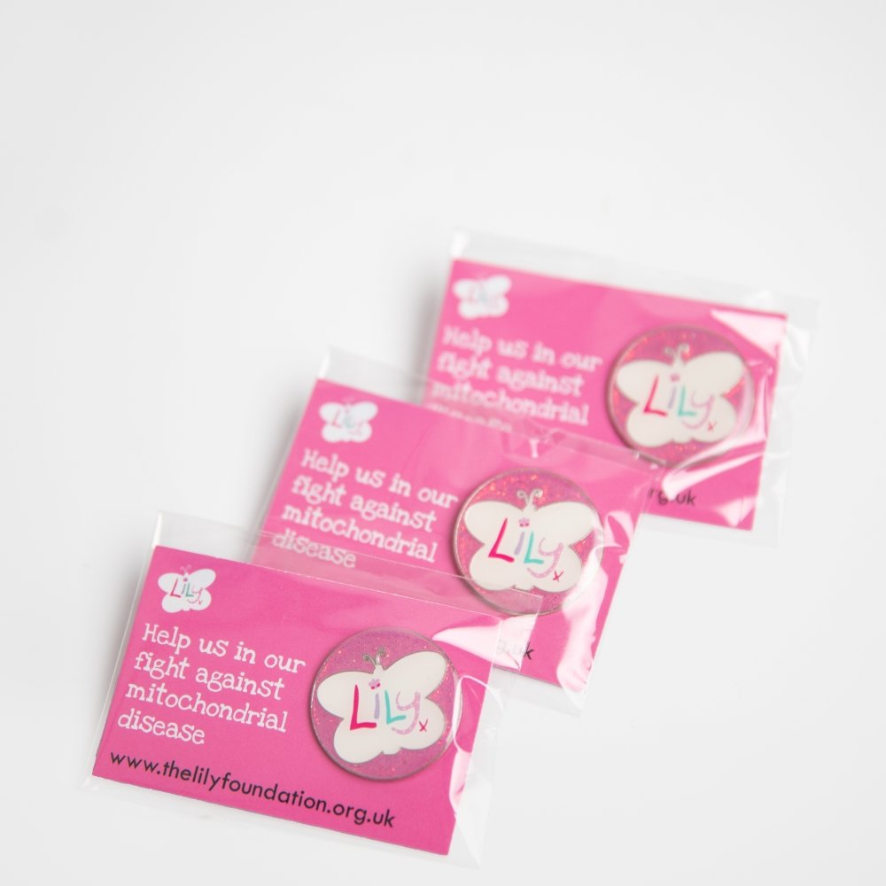 Three glittery pink enamel badges featuring the Lily Foundation logo on backing boards.