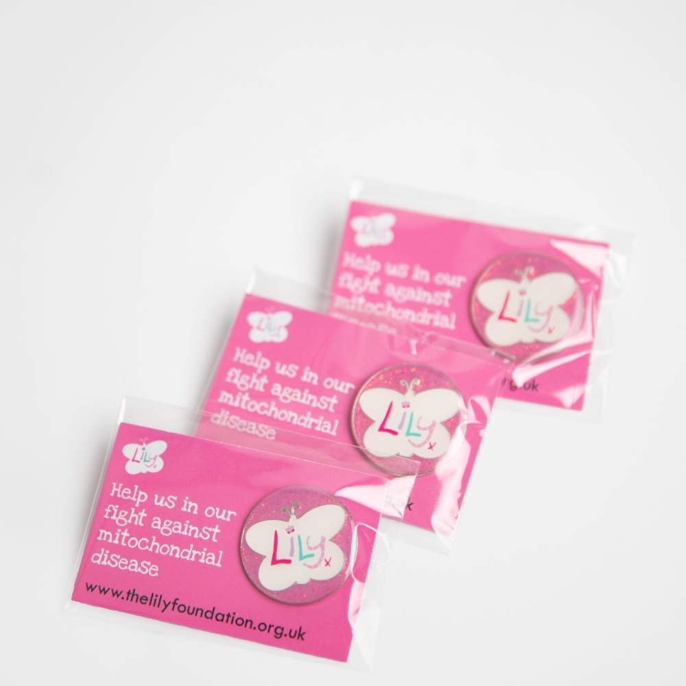 Three glittery pink enamel badges featuring the Lily Foundation logo on backing boards.