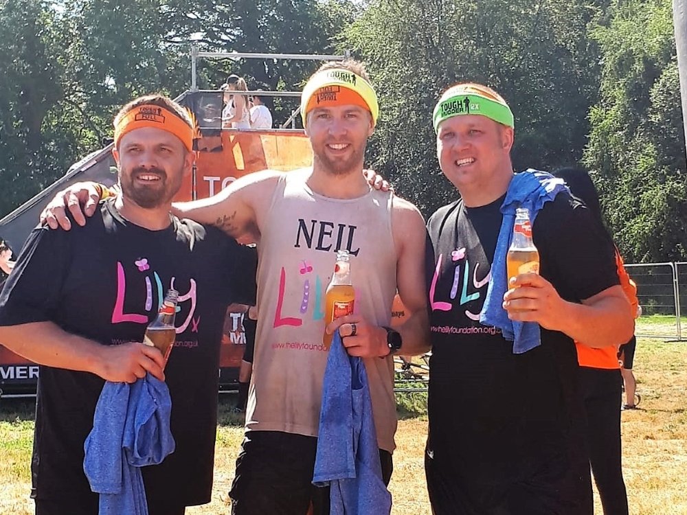 Tough Mudder London South 15k 2025 - Three men in Lily Foundation tops smiling at the end of a Tough Mudder events