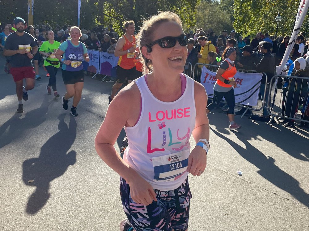 Royal Parks Half Marathon 2024 - Lady in a Lily Foundation vest and sunglasses running and smiling