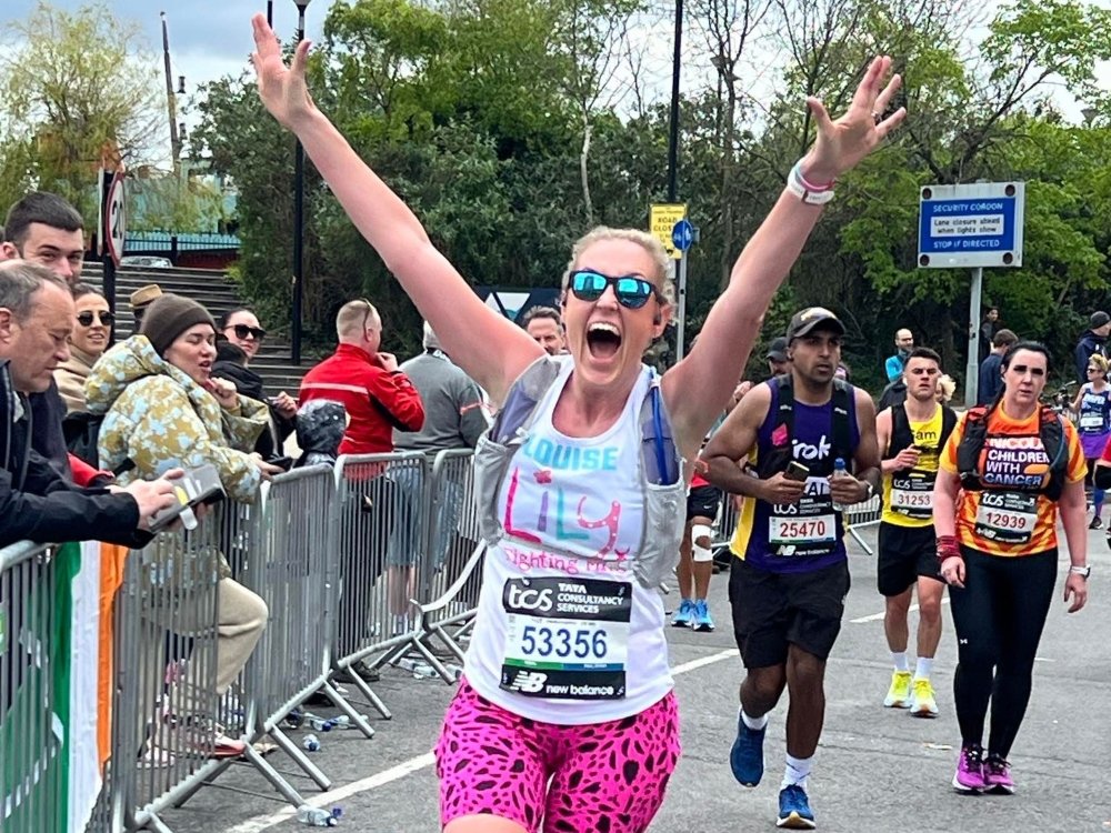 A woman in a Lily top with her hands raised in the air running the London Marathon