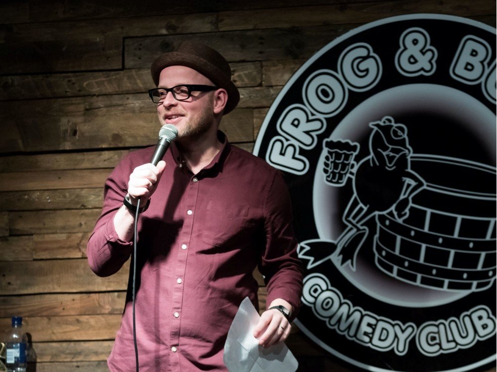 A comedian standing on stage with a mic at the Frog and Bucket Comedy Club Manchester