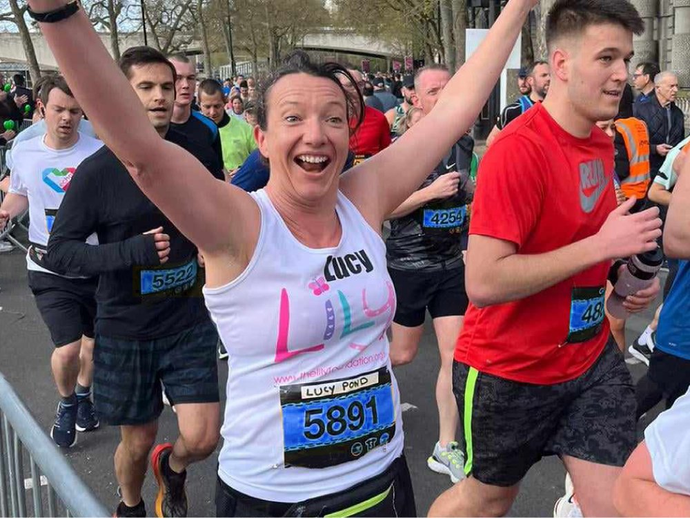 Bath Half Marathon 2026 - A lady wearing a Lily Foundation top running with her arms in the air