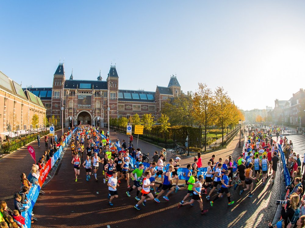 Amsterdam Marathon - Large group of runners coming down a road and turning a corner onto an Amsterdam canal