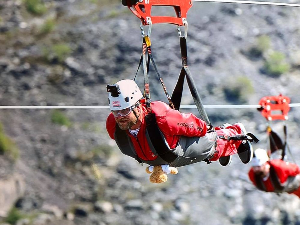 A man in a white crash helmet suspended from a zip wire