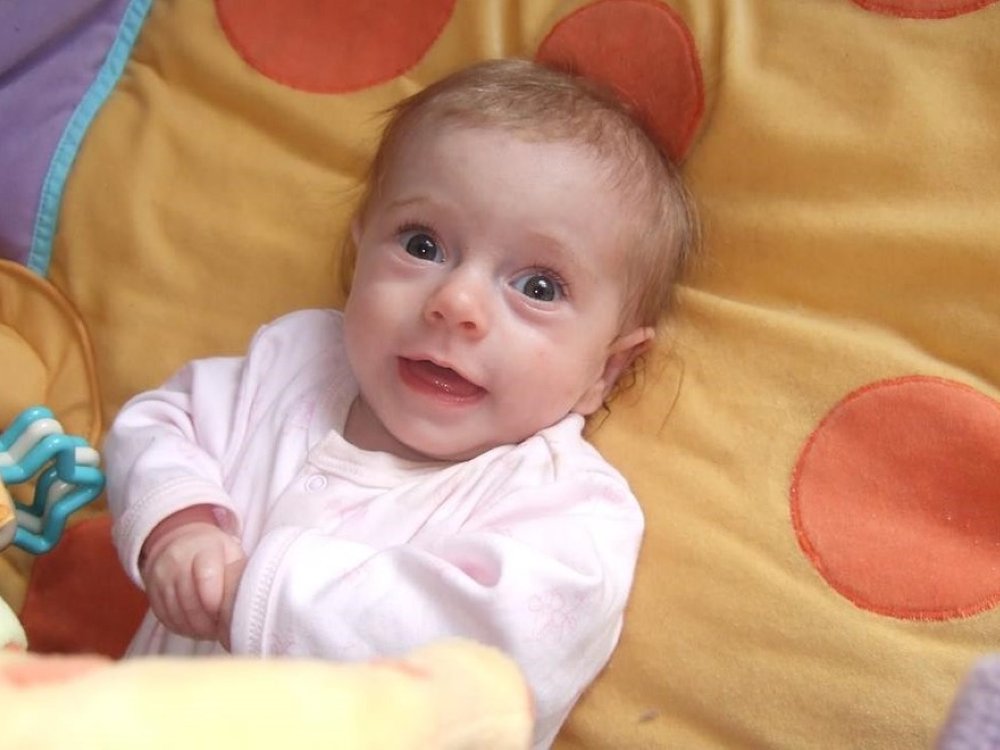 Baby lily with blonde hair smiling on a yellow and orange blanket