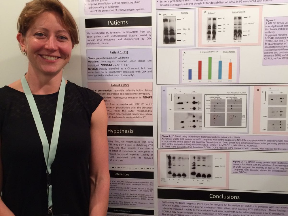 A lady with short hair and a lanyard standing in front of a poster