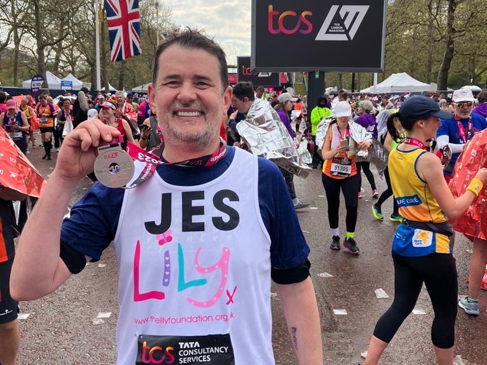 A man in a Lily vest grinning and holding up his finishers medal