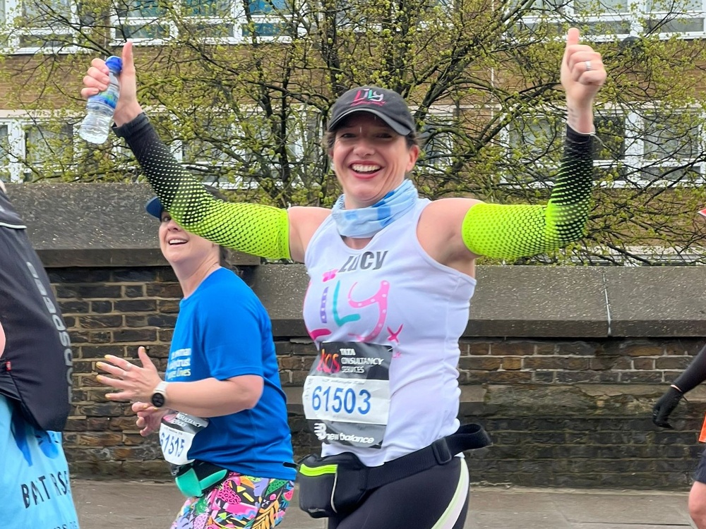 A woman in a Lily vest smiling and running with her arms raised