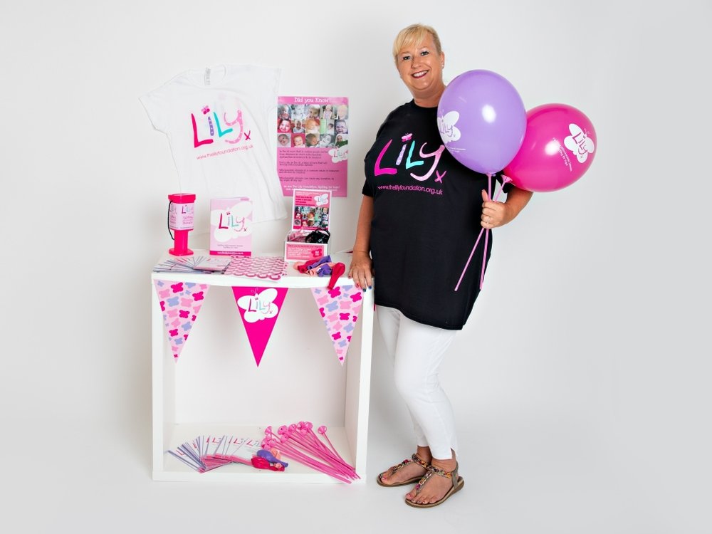 A woman in a Lily top standing next to a table with bunting, balloons and leaflets