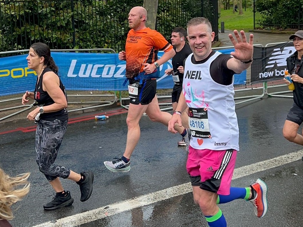 A man in a Lily vest waves as he runs past the camera