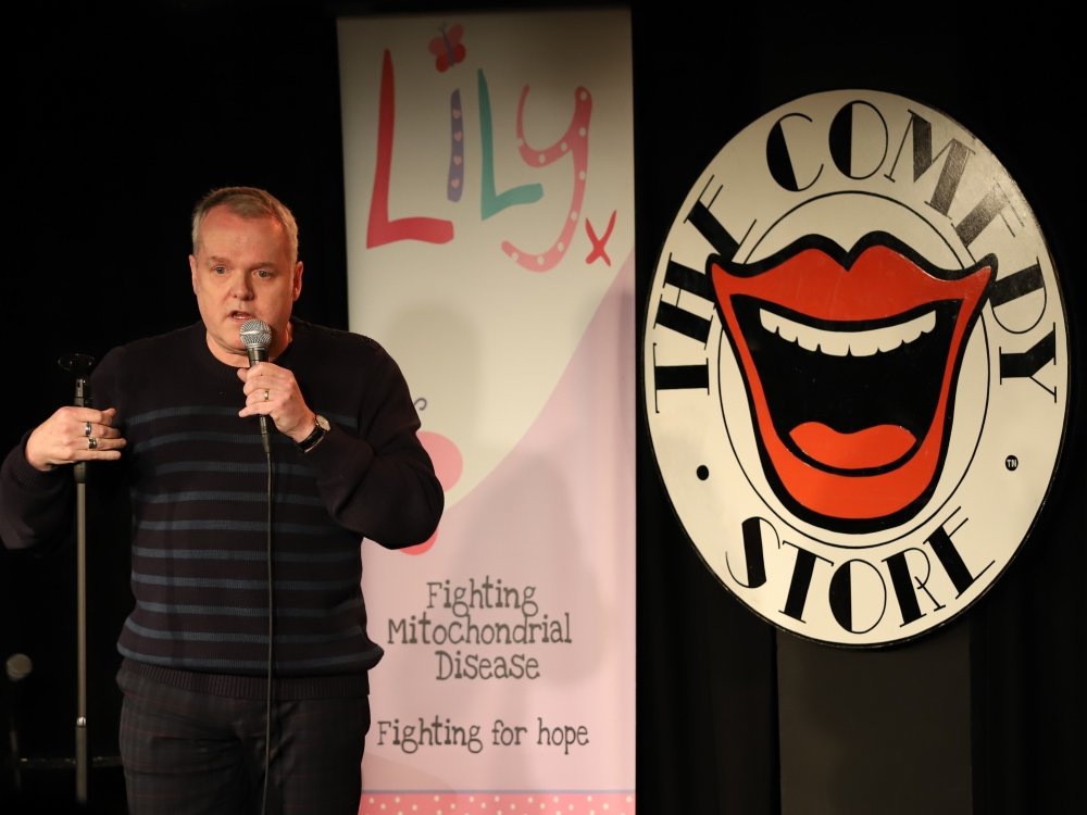 Comedian Kevin Day standing in front of a Lily banner and holding a microphone