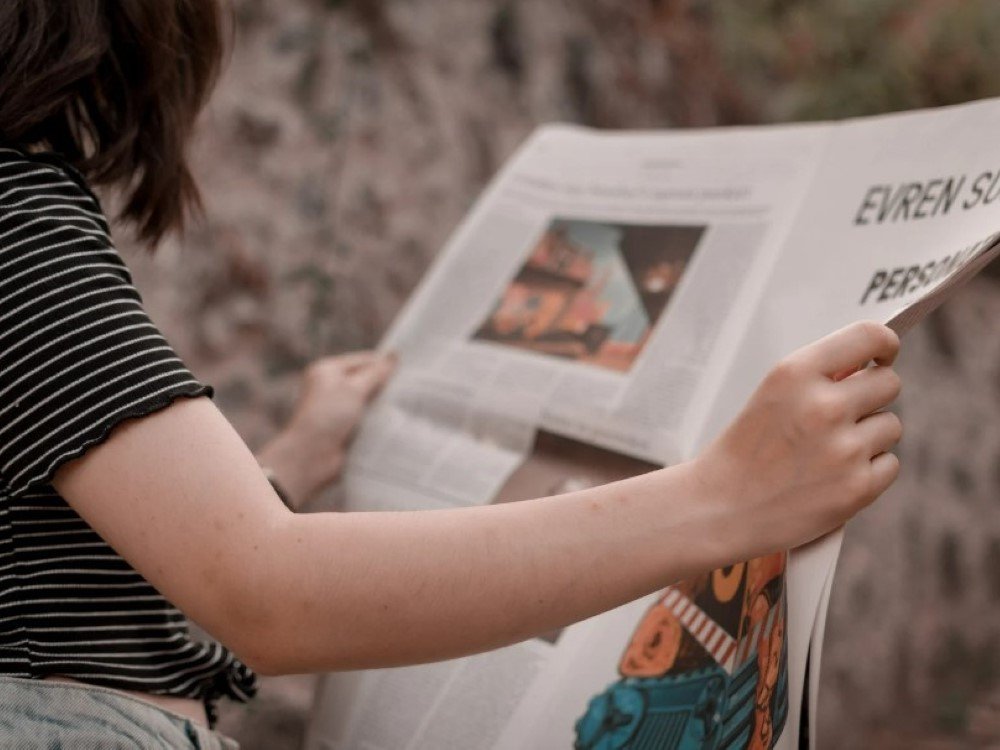 A lady holding an open newspaper and reading it