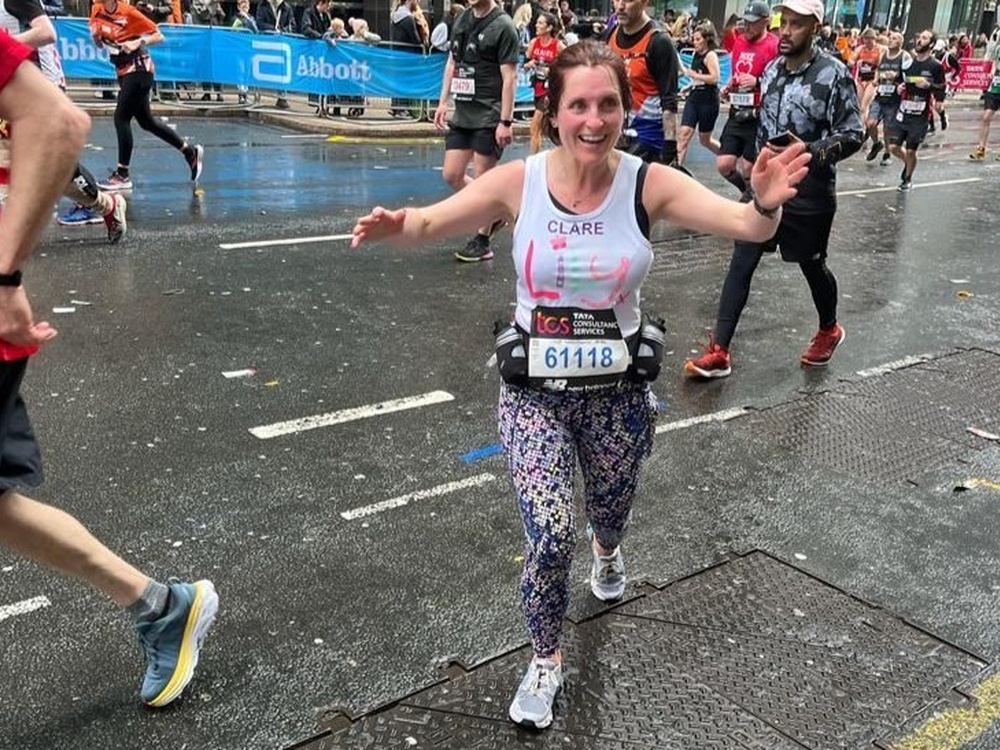 A lady in a Lily vest runs with her arms raised in the air