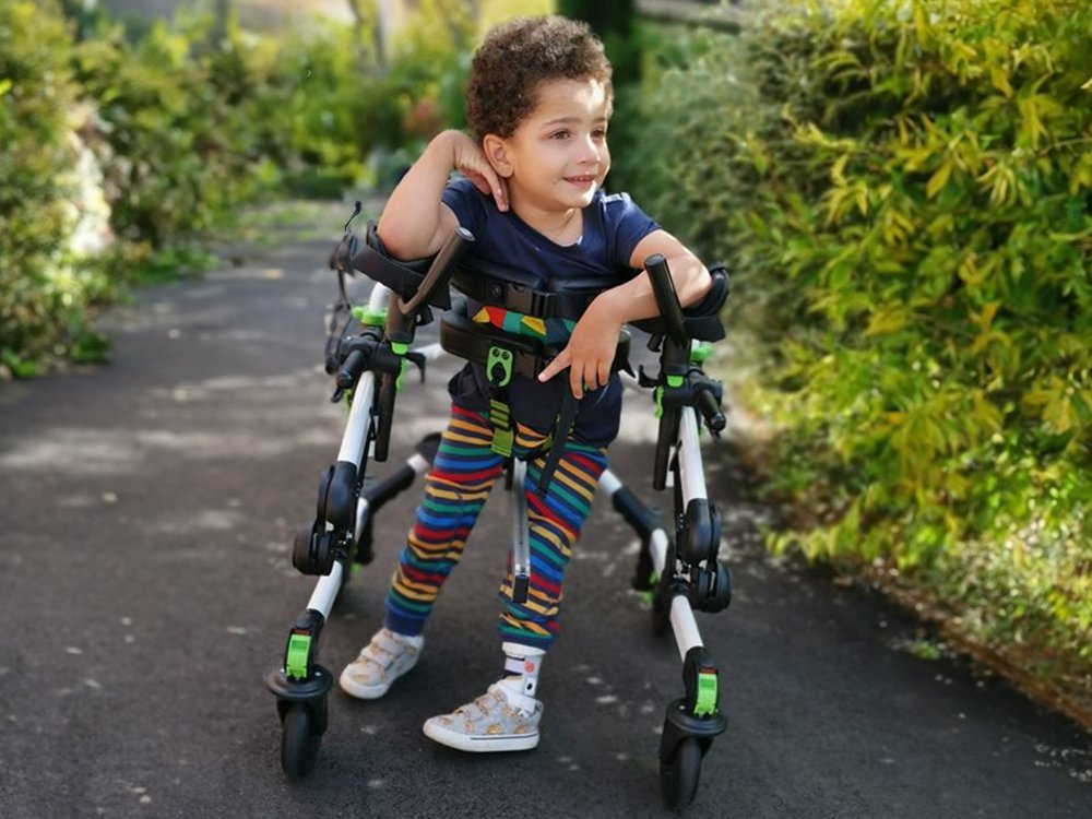 smiley young boy with mito, walking down a sunny lane with the assistance of a walking frame