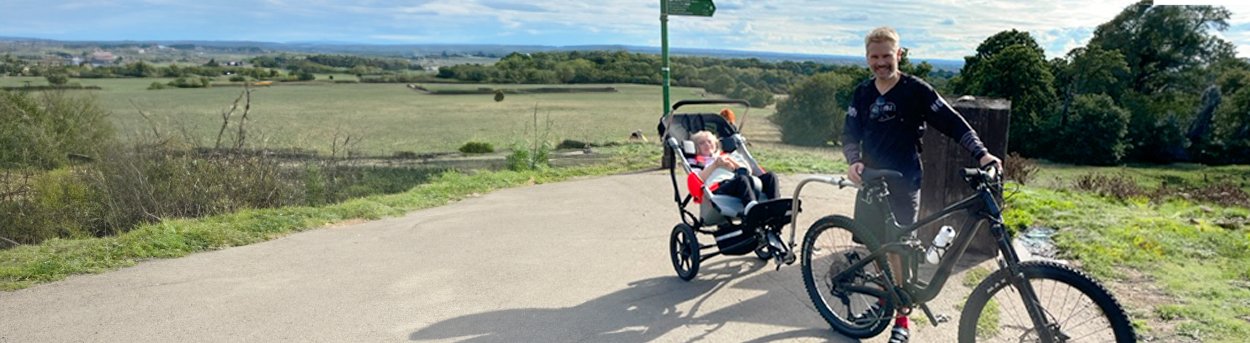 Dad on mountain bike, towing his daughters adjusted wheelchair. stopped at the top of a hill to enjoy the view