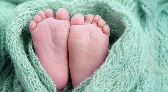 Green and lilac soft blanket wrapped in a love heart shape around a pair of tiny baby feet