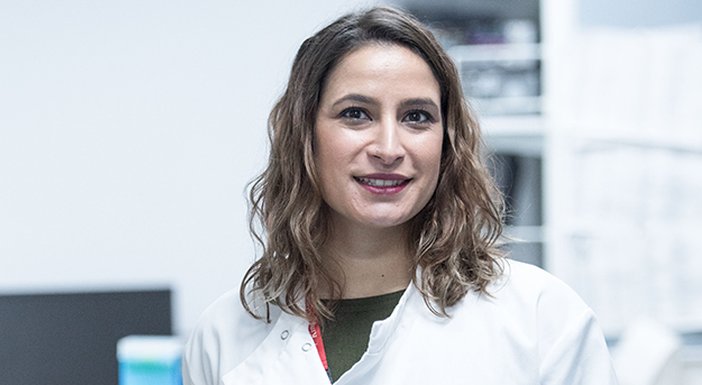 Lily researcher in a white lab coat standing at a bench full of research equipment