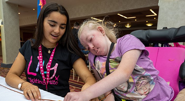 Two girls, one in a Lily t-shirt and lanyard, the other in a wheelchair, working at a table