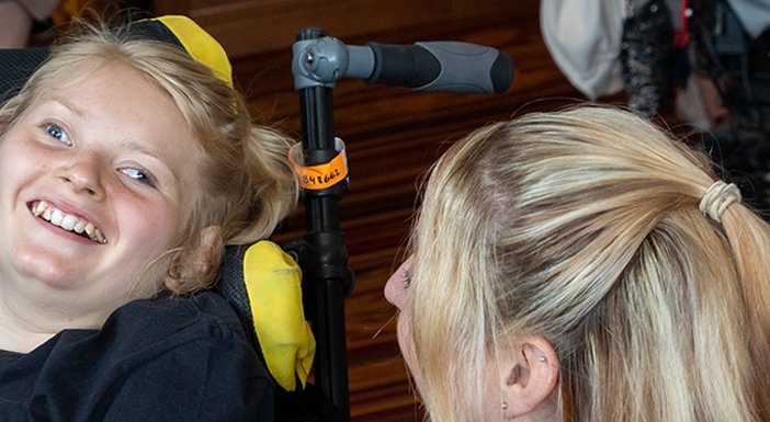 Young girl, who has mitochondrial disease, laughing with her mum and dad from her wheelchair