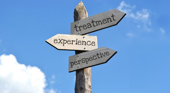 A road sign with blue sky behind with the words treatment, experience and perspective