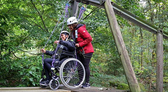 Young adult in her wheelchair being pushed by her mum over a forest assault course