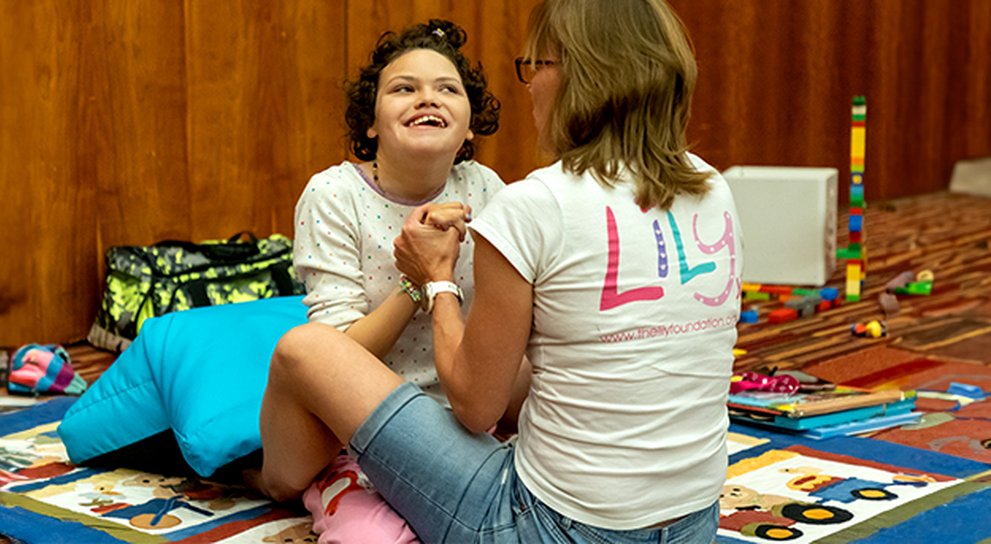 Young mito patient on a mat surrounded by play items at the Lily Family Support Weekend