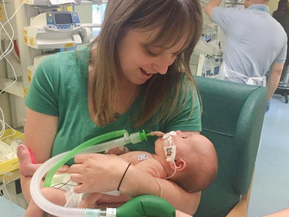 A women cradling and look down on a small baby with a breathing tube