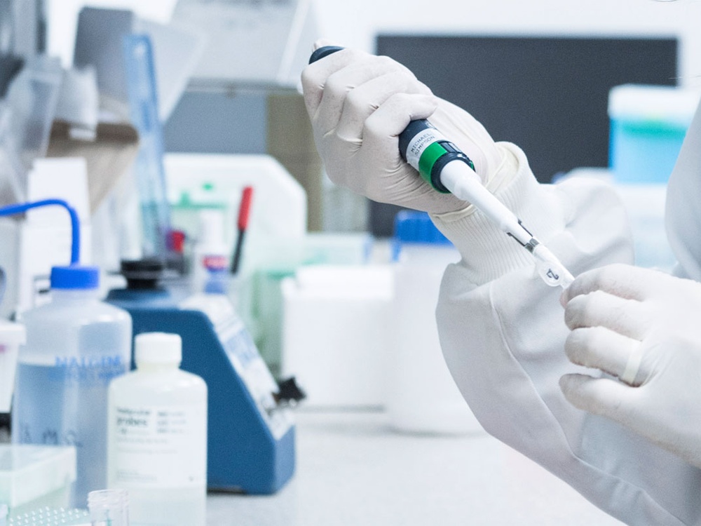 Scientist in a research lab, wearing white rubber gloves and testing samples