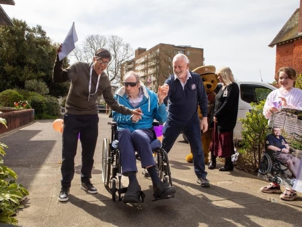 A man in a wheelchair holding his arm up with others standing around him