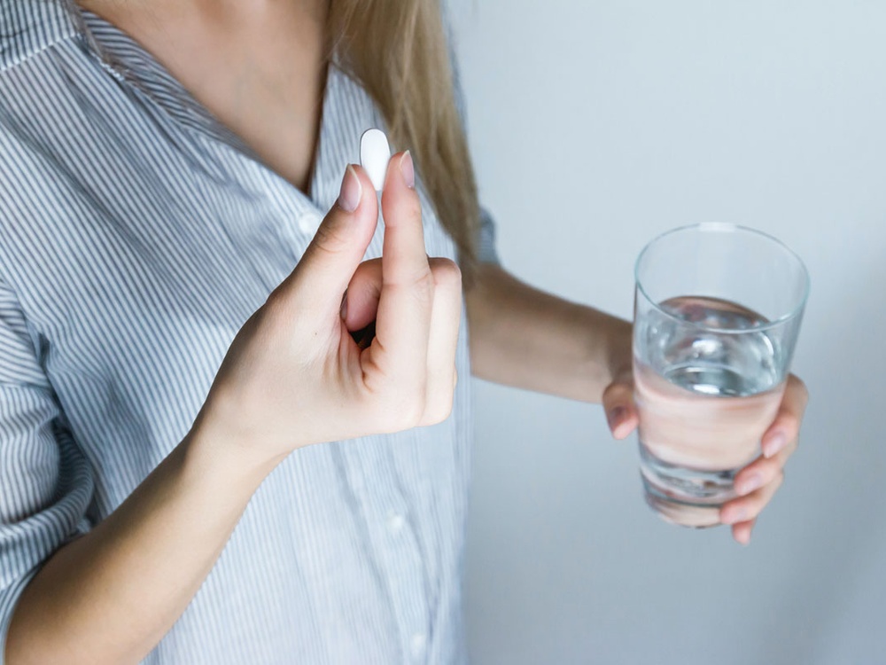 An adult is holding a pill in one hand and a glass of water in the other