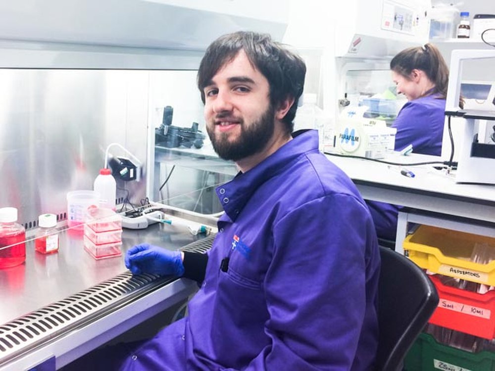 A man in a blue lab coat sat in front of airflow cabinet